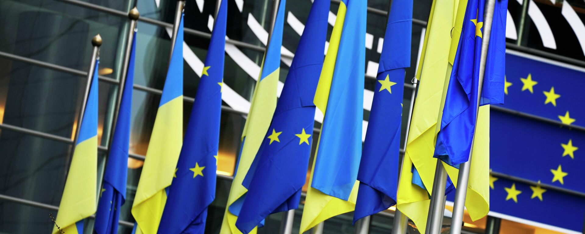 Bandeiras da Ucrânia e da União Europeia (UE) penduradas juntas no exterior do edifício antes de uma sessão plenária extraordinária sobre a Ucrânia no Parlamento Europeu em Bruxelas, 1º de março de 2022 - Sputnik Brasil, 1920, 04.12.2023