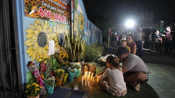 Uma família acende uma vela em um memorial improvisado na creche Cantinho do Bom Pastor após um ataque fatal a crianças em Blumenau, Brasil, 5 de abril de 2023 - Sputnik Brasil