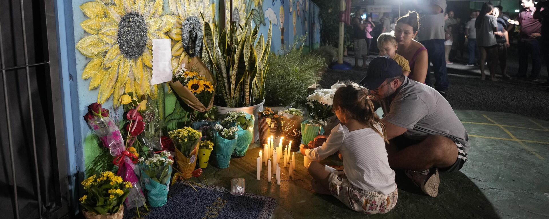 Uma família acende uma vela em um memorial improvisado na creche Cantinho do Bom Pastor após um ataque fatal a crianças em Blumenau, Brasil, 5 de abril de 2023 - Sputnik Brasil, 1920, 08.04.2023