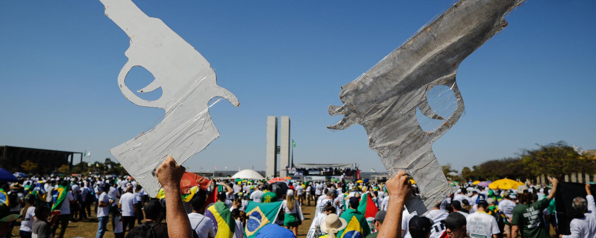 Um homem segura dois sinais em forma de arma durante uma manifestação pró-armas em apoio ao presidente brasileiro Jair Bolsonaro em Brasíli, em 9 de julho de 2021 - Sputnik Brasil, 1920, 25.04.2023