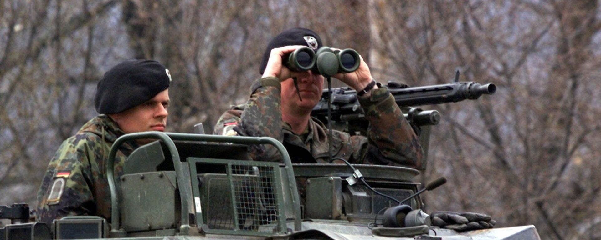 Um oficial alemão do contingente da OTAN implantado na Macedônia olha através de seus binóculos, enquanto sua unidade blindada está posicionada perto de Tetovo, perto da fronteira da província iugoslava de Kosovo, 50 quilômetros a noroeste de Skopje, 29 de março de 1999 - Sputnik Brasil, 1920, 08.05.2023