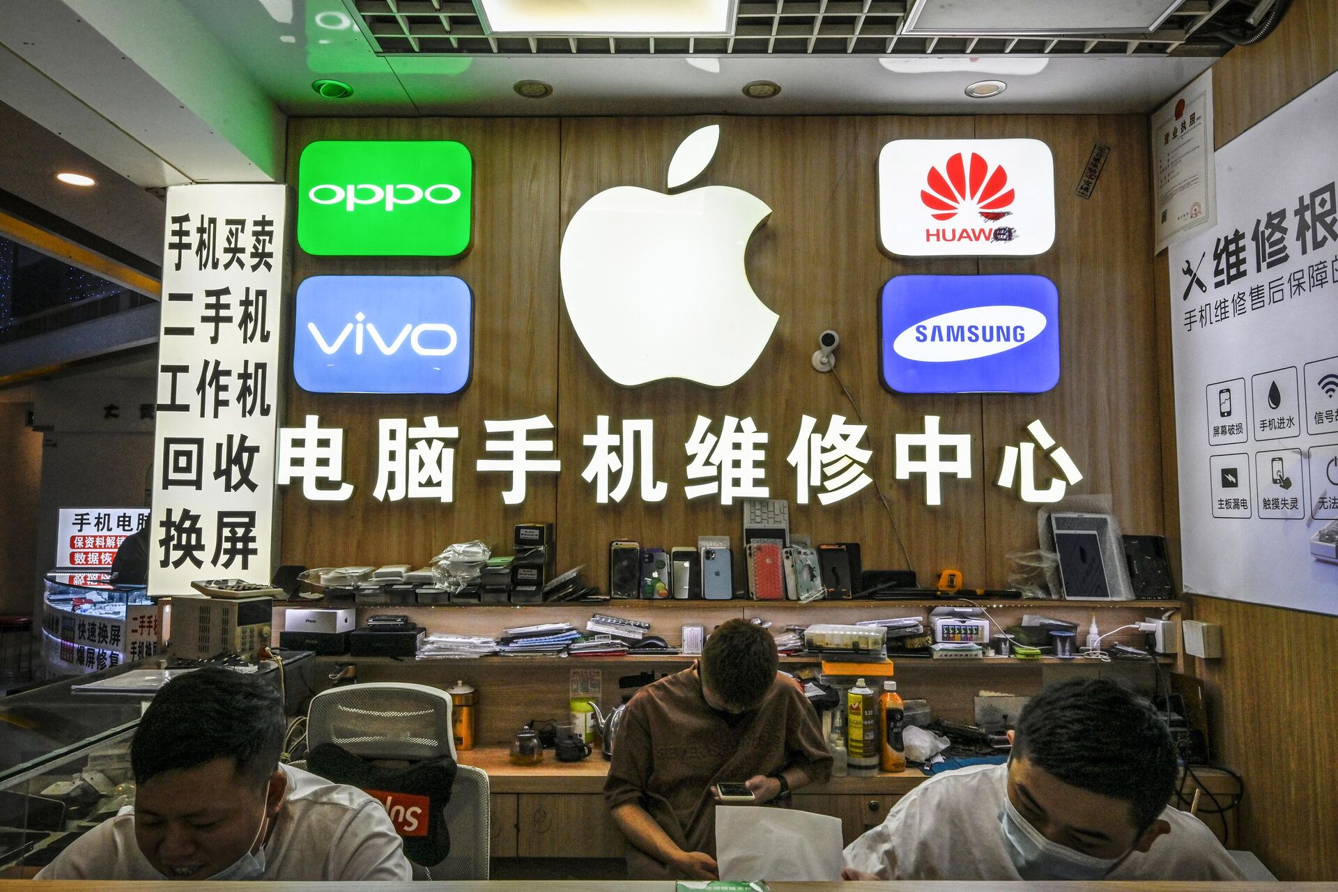 Funcionários trabalhando em uma loja com logotipos de fabricantes de smartphones, incluindo Apple, Huawei, Oppo, Vivo e Samsung, no mercado de eletrônicos Huaqiangbei, em Shenzhen, China, 12 de julho de 2022 - Sputnik Brasil, 1920, 06.07.2023