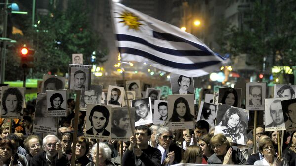Manifestantes, um deles agitando uma bandeira uruguaia, carregam cartazes com imagens de pessoas desaparecidas durante a ditadura uruguaia de 1973-85 durante uma marcha em Montevidéu, Uruguai - Sputnik Brasil