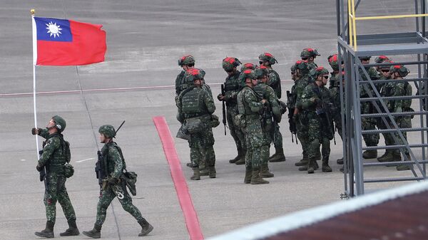 Um soldado taiwanês segura uma bandeira nacional de Taiwan perto de um grupo de soldados com marcas vermelhas em seus capacetes para desempenhar o papel de inimigo durante os exercícios militares anuais de Han Kuang, simulando um ataque a um campo de aviação no Aeroporto Internacional de Taoyuan, em Taoyuan, norte de Taiwan, julho 26, 2023 - Sputnik Brasil