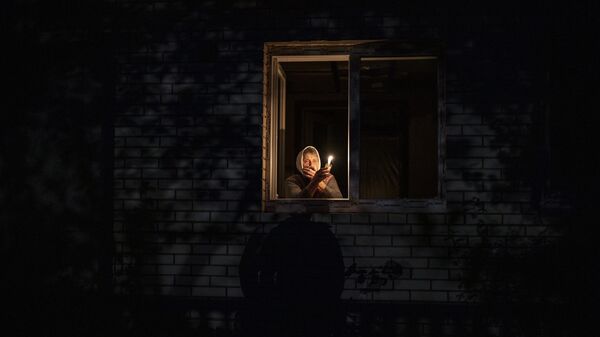 Mulher olha pela janela enquanto segura uma vela para iluminar sua casa durante uma queda de energia em Kiev. Ucrânia, 20 de outubro de 2022 - Sputnik Brasil