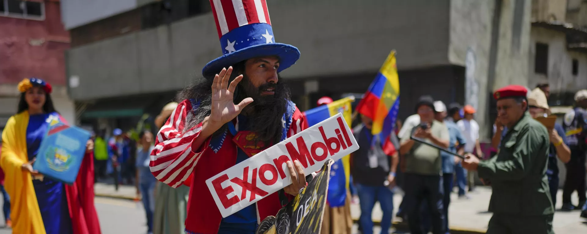 Homem vestido como o personagem norte-americano Tio Sam segura uma placa da petrolífera ExxonMobil durante a marcha pró-governo chamada Recupere Essequibo, em Caracas. Venezuela, 26 de setembro de 2023 - Sputnik Brasil, 1920, 26.09.2023