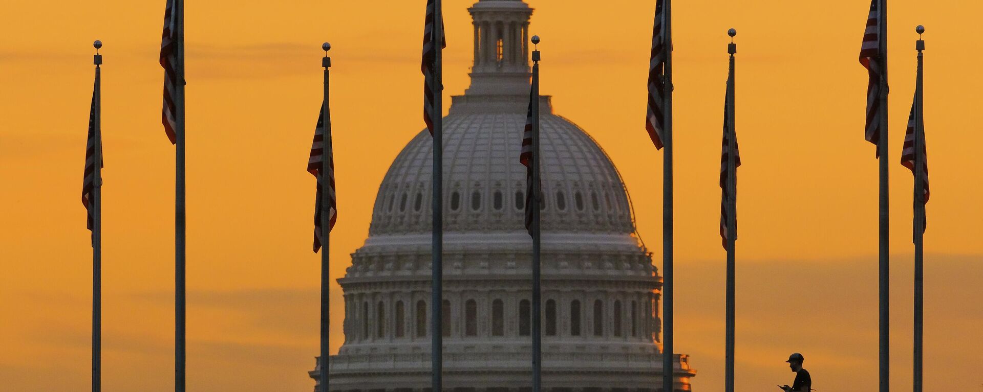 Pedestre caminha ao nascer do sol por bandeiras dos EUA no National Mall e passa pelo edifício do Capitólio norte-americano, em Washington D.C. EUA, 7 de novembro de 2022 - Sputnik Brasil, 1920, 01.10.2023