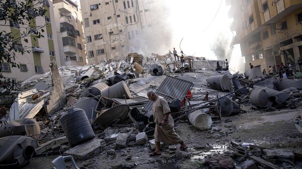 Palestinos caminham sobre escombros de prédio atingido por bombardeio israelense em 7 de outubro de 2023 - Sputnik Brasil