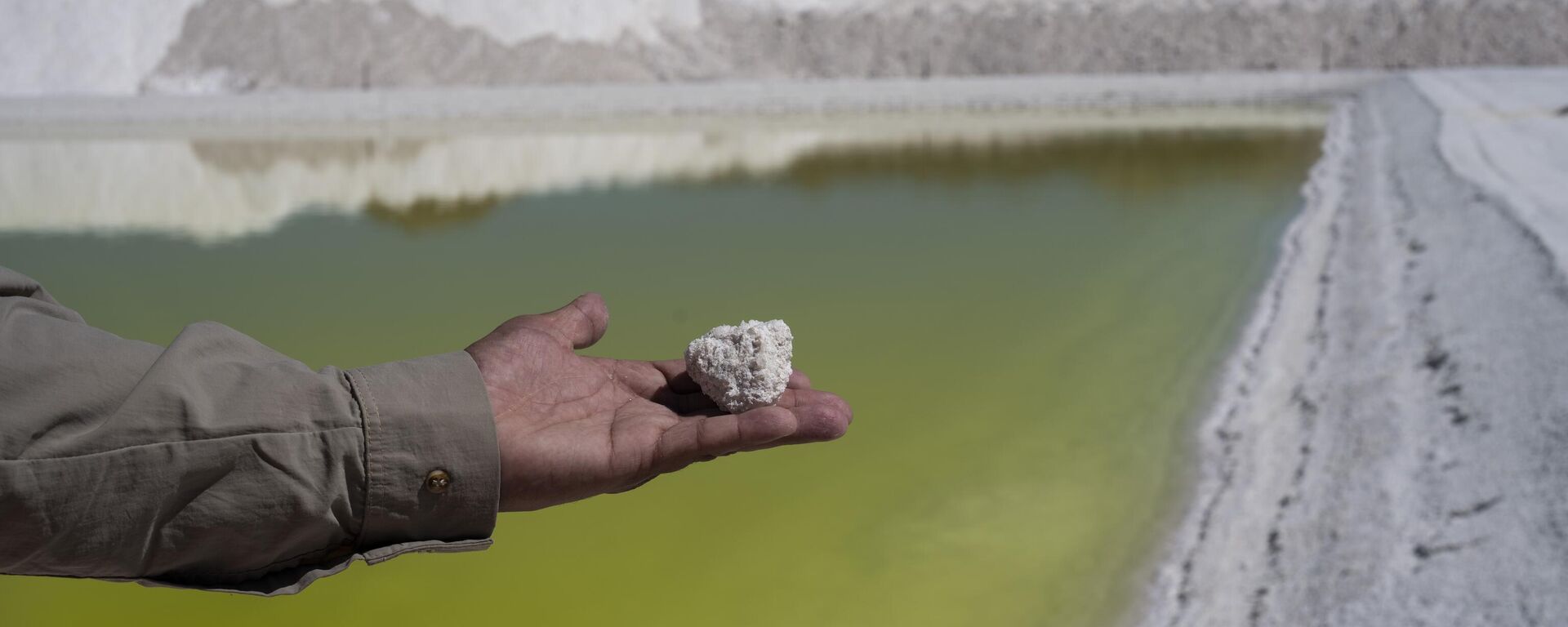 Trabalhador da mina de lítio Albemarle mostra pedaço de sal perto de uma piscina de salmoura altamente concentrada em lítio no Deserto do Atacama. Chile, 17 de abril de 2023 - Sputnik Brasil, 1920, 12.10.2023