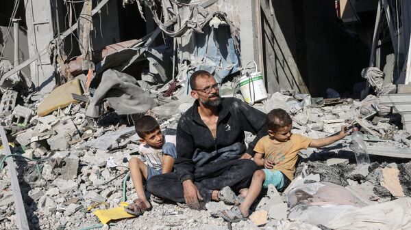 Homem palestino sentado com membros de sua família do lado de fora de um prédio destruído por um ataque aéreo israelense em Rafah, no sul da Faixa de Gaza, em 12 de outubro de 2023 - Sputnik Brasil