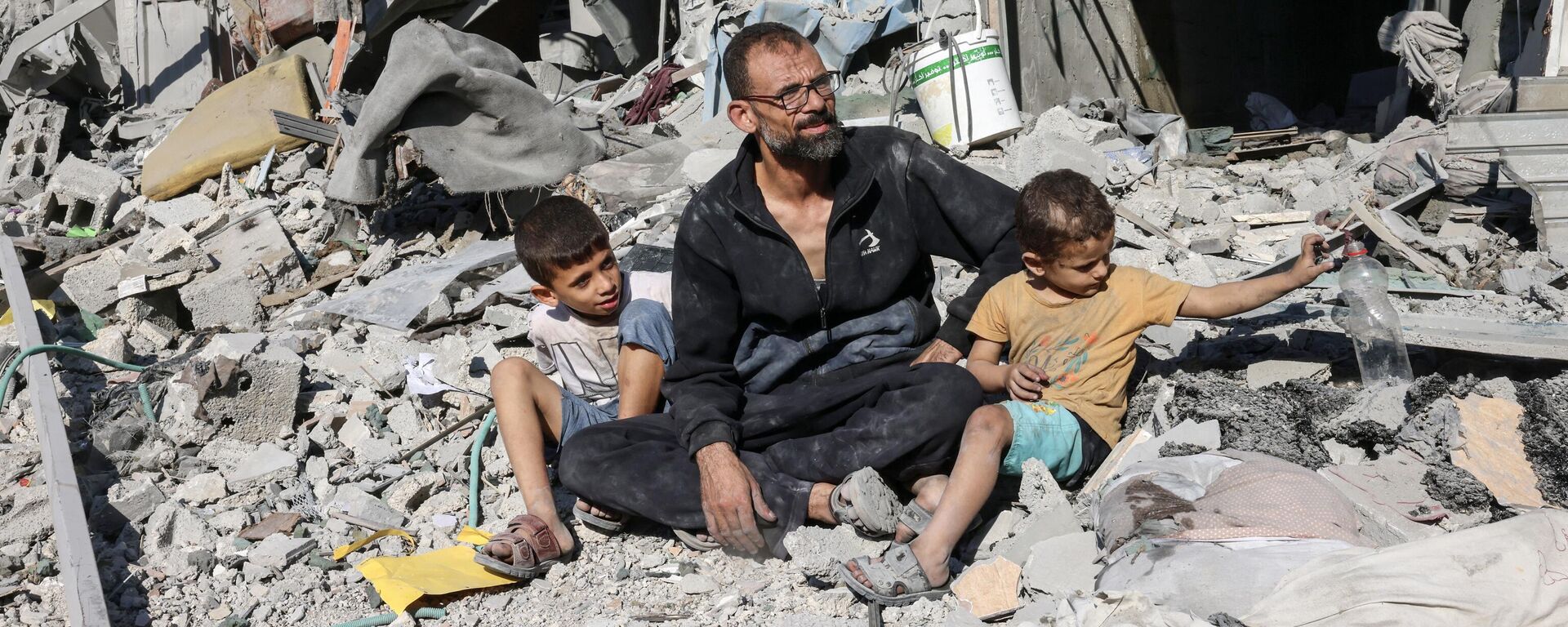 Homem palestino sentado com membros de sua família do lado de fora de um prédio destruído por um ataque aéreo israelense em Rafah, no sul da Faixa de Gaza, em 12 de outubro de 2023 - Sputnik Brasil, 1920, 12.10.2023
