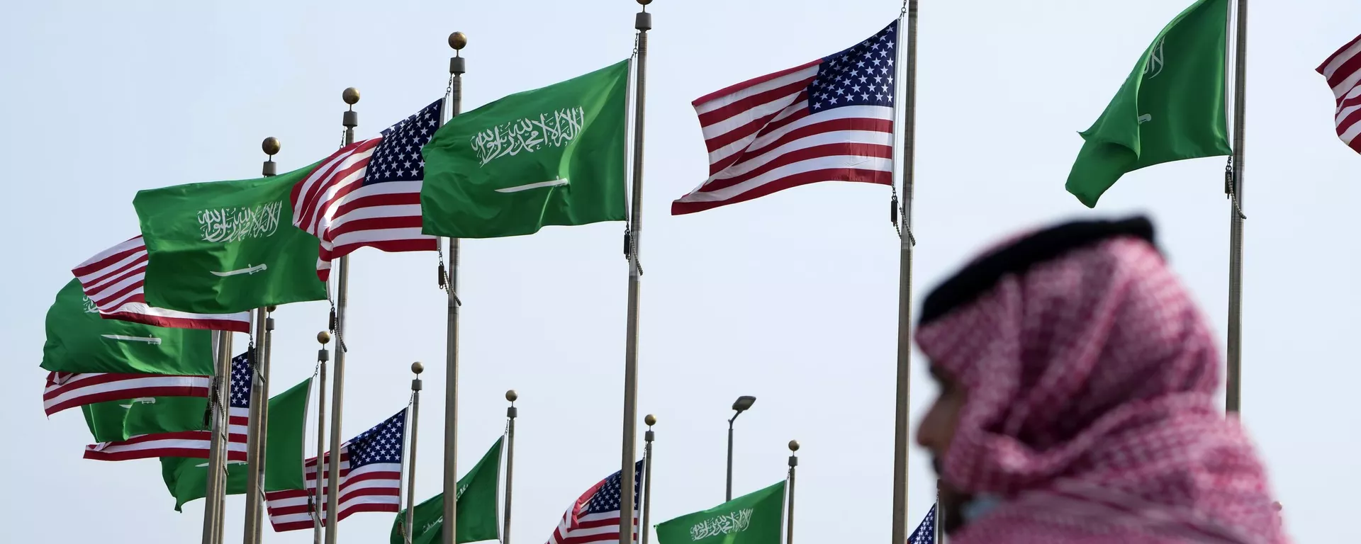 Um homem sob as bandeiras dos EUA e da Arábia Saudita antes da visita do presidente dos EUA, Joe Biden, em uma praça em Jeddah, Arábia Saudita, 14 de julho de 2022 - Sputnik Brasil, 1920, 17.10.2023