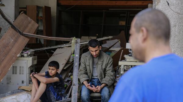 Palestinos sentam-se nas ruínas de uma casa após um recente bombardeio nas ruas da Cidade de Gaza, na Palestina. - Sputnik Brasil