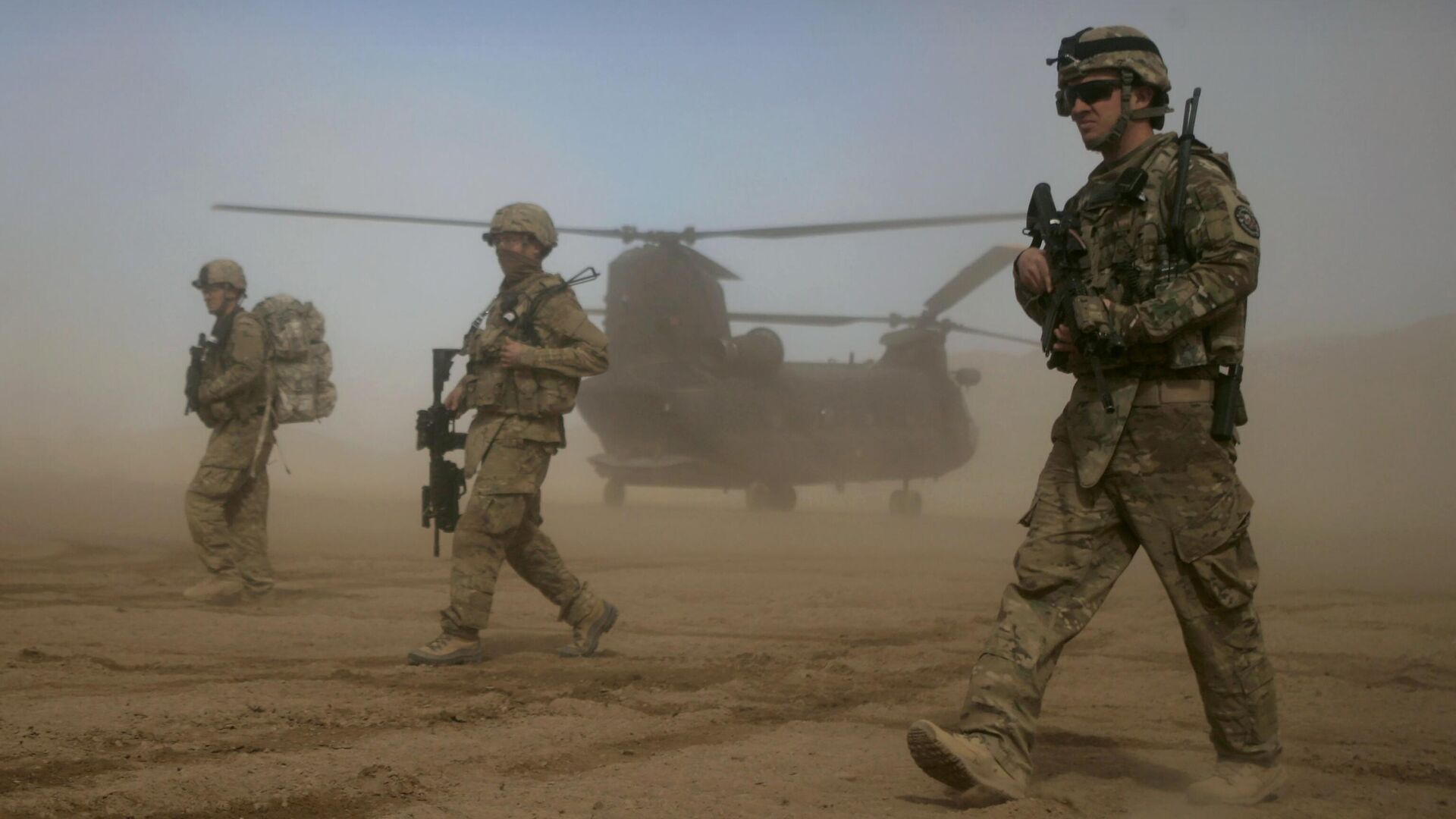 Soldados dos EUA, parte da Força Internacional de Assistência à Segurança (ISAF, na sigla em inglês) liderada pela Organização do Tratado do Atlântico Norte (OTAN), caminham enquanto um helicóptero Chinook dos EUA é visto ao fundo em Shindand, Herat, a oeste de Cabul, Afeganistão, 28 de janeiro de 2012 - Sputnik Brasil, 1920, 02.11.2023