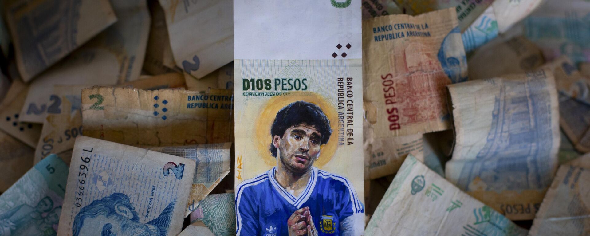 Uma peça arte do artista Sergio Díaz apresenta a falecida lenda do futebol Diego Maradona com as mãos envoltas em um rosário e uma auréola atrás da cabeça, pintada em uma nota de dez pesos argentinos em 9 de setembro de 2023 - Sputnik Brasil, 1920, 02.11.2023