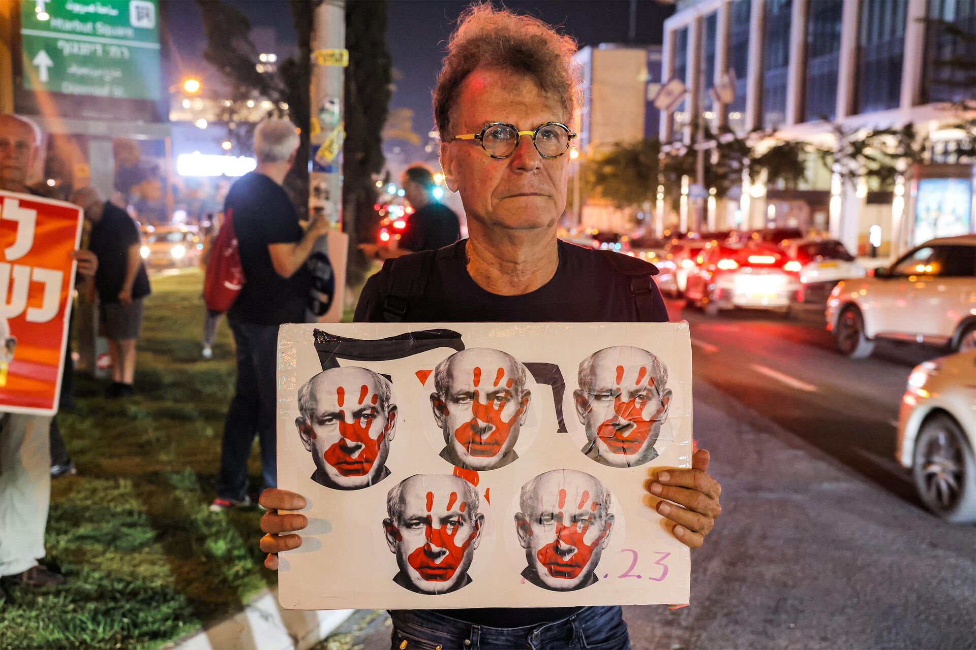 Um homem com uma placa mostrando cinco rostos do primeiro-ministro israelense Benjamin Netanyahu manchados com marcas de mãos vermelhas durante um protesto pedindo a libertação de reféns mantidos por militantes palestinos desde o ataque de 7 de outubro, em Tel Aviv, em 28 de outubro de 2023 - Sputnik Brasil, 1920, 03.11.2023
