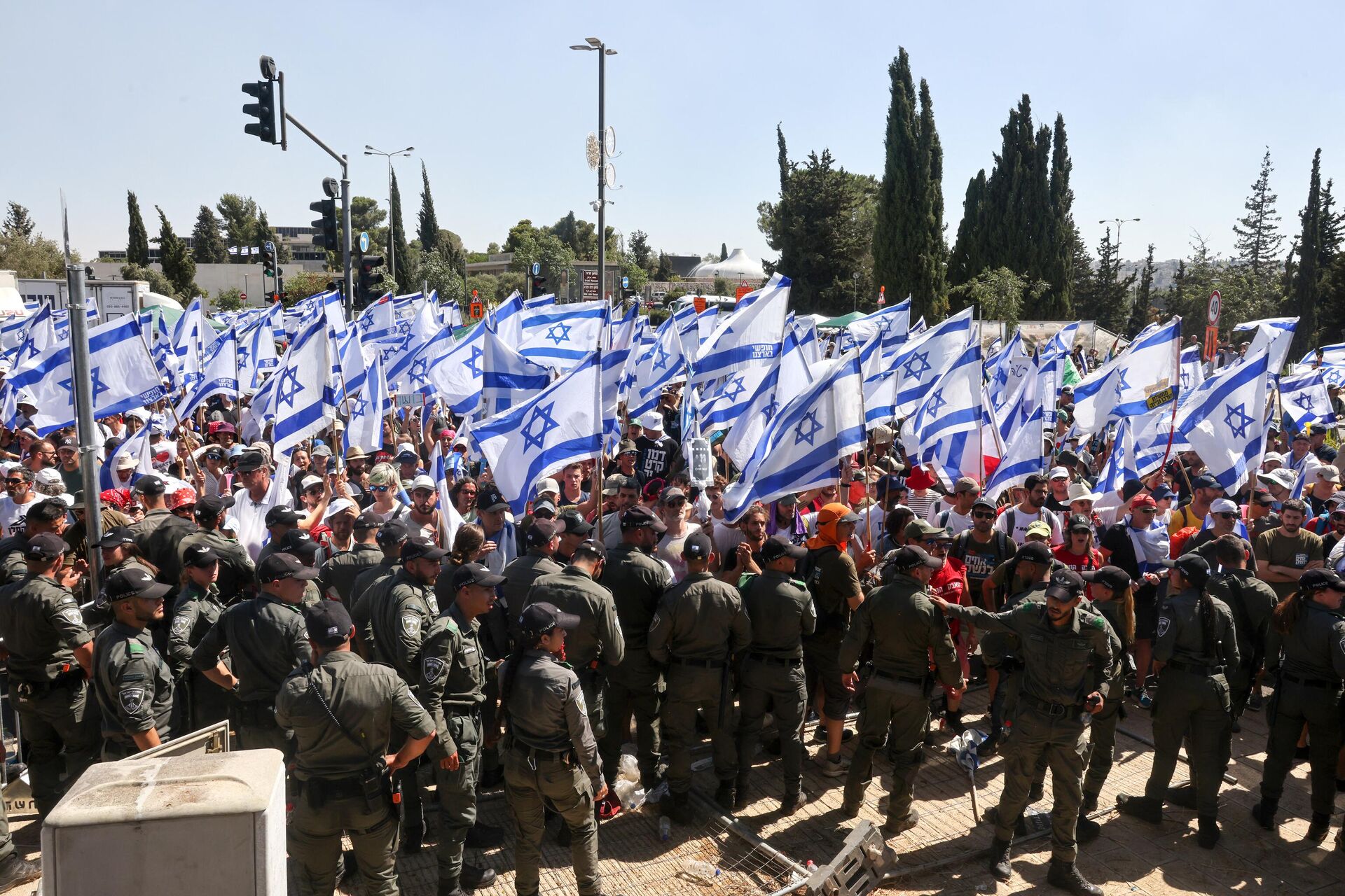 Forças de segurança israelenses montam guarda enquanto manifestantes agitam a bandeira nacional na entrada do Knesset em meio a uma onda de protestos que durou meses contra a planejada reforma judicial do governo,  em 24 de julho de 2023 - Sputnik Brasil, 1920, 03.11.2023