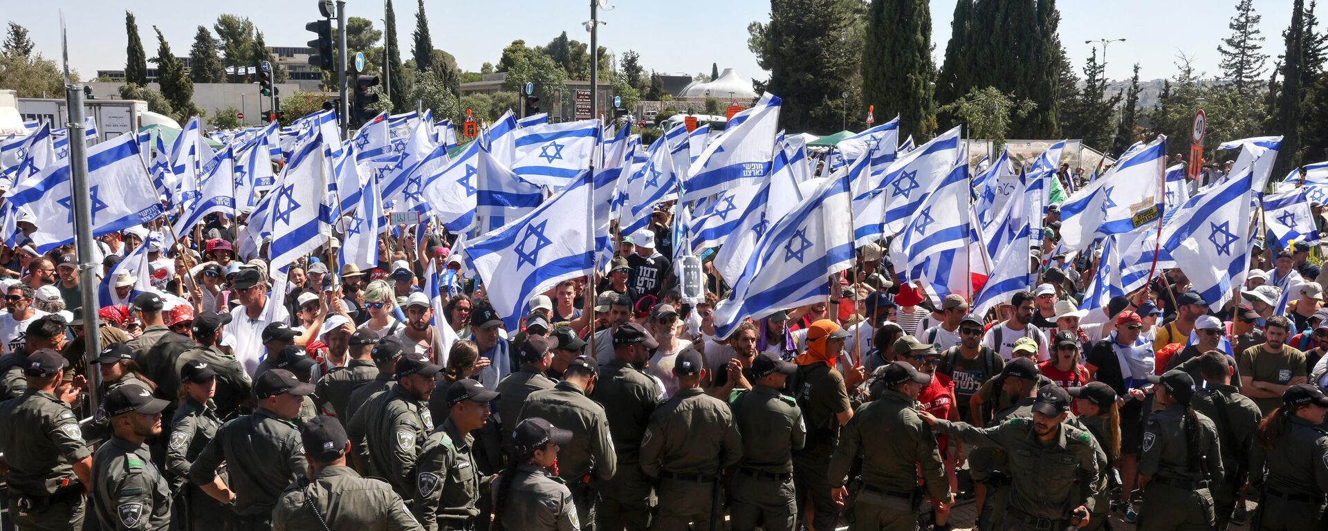 Forças de segurança israelenses montam guarda enquanto manifestantes agitam a bandeira nacional na entrada do Knesset em meio a uma onda de protestos que durou meses contra a planejada reforma judicial do governo,  em 24 de julho de 2023 - Sputnik Brasil, 1920, 24.11.2023