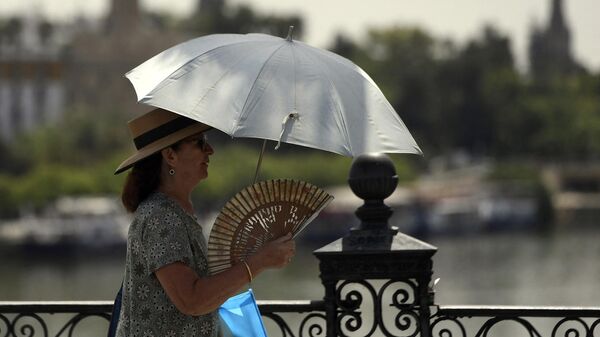Uma mulher usa guarda-chuva e leque para se proteger do sol e das altas temperaturas em Sevilha, 7 de agosto de 2023 - Sputnik Brasil