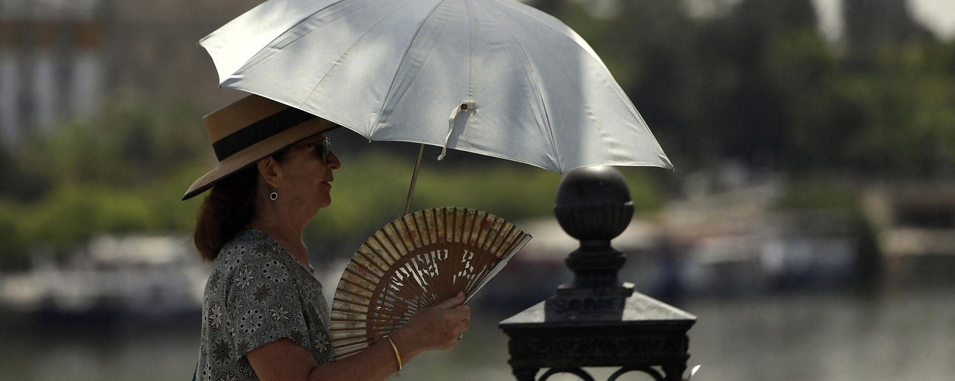 Uma mulher usa guarda-chuva e leque para se proteger do sol e das altas temperaturas em Sevilha, 7 de agosto de 2023 - Sputnik Brasil, 1920, 08.11.2023