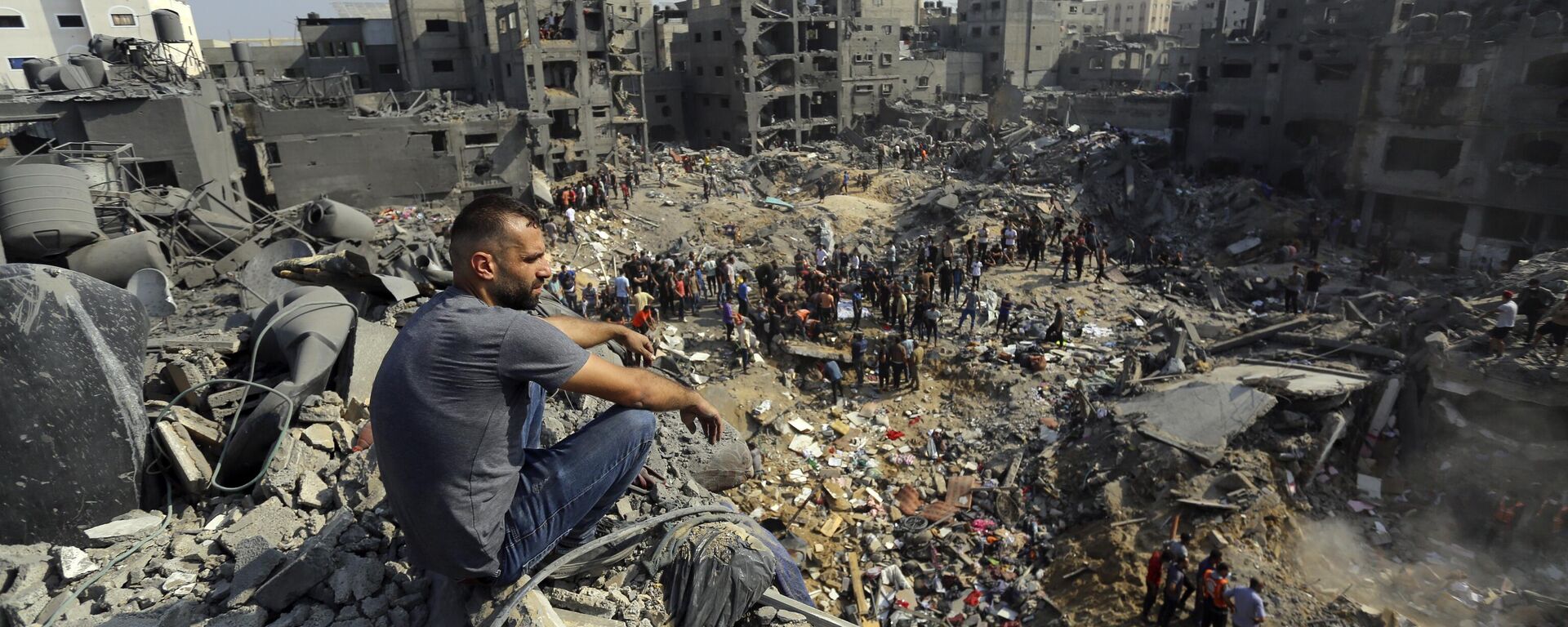 Homem sentado nos escombros enquanto outros vagam entre os destroços de edifícios que foram alvo de ataques aéreos israelenses no campo de refugiados de Jabaliya, norte da Faixa de Gaza, em 1º de novembro de 2023 - Sputnik Brasil, 1920, 29.11.2023