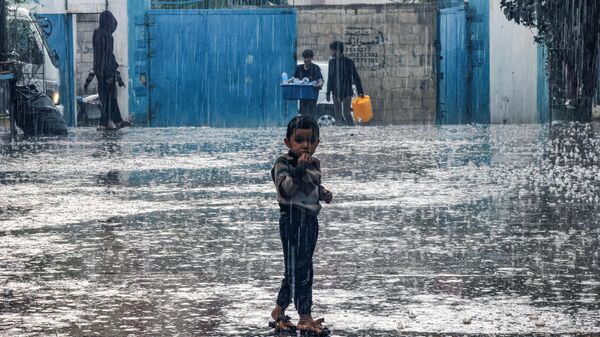 Um menino fica na chuva em uma escola administrada pela Agência das Nações Unidas de Agência das Nações Unidas de Assistência aos Refugiados da Palestina no Próximo Oriente (UNRWA, na sigla em inglês), em Rafah. Faixa de Gaza, 14 de novembro de 2023 - Sputnik Brasil