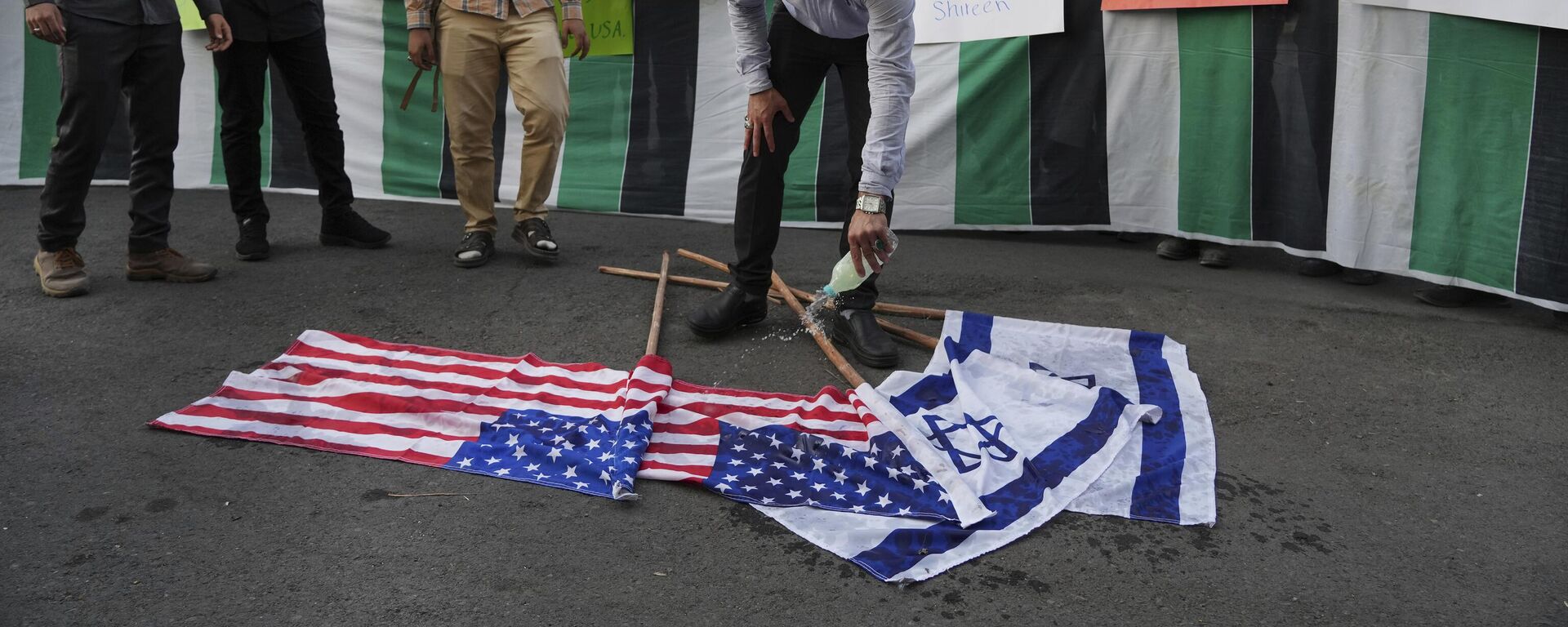Manifestante derrama gasolina nas bandeiras de Israel e dos EUA, antes de atear fogo a elas, durante um protesto em Teerã contra a viagem de Biden ao Oriente Médio. Irã, 16 de julho de 2022 - Sputnik Brasil, 1920, 01.04.2024