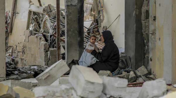 Uma mulher palestina segura seu bebê entre os escombros de edifícios destruídos na Cidade de Gaza, em 25 de novembro de 2023 - Sputnik Brasil