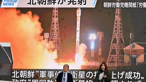 Pedestres passam por tela que exibe lançamento do Malligyong-1, um satélite de reconhecimento da Coreia do Norte, em Tóquio, Japão, 22 de novembro de 2023 - Sputnik Brasil