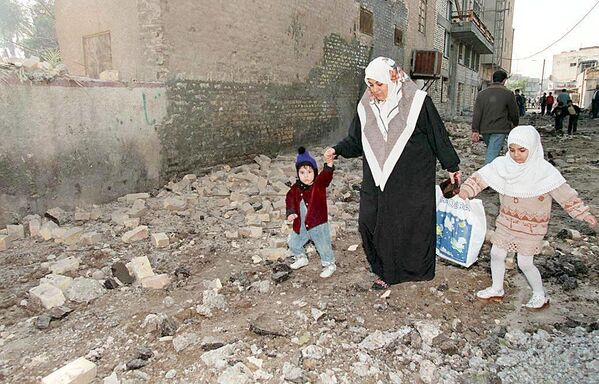 Mulher iraquiana ajuda os seus filhos a caminhar sobre os escombros resultantes dos ataques aéreos noturnos americanos e britânicos em Bagdá. - Sputnik Brasil
