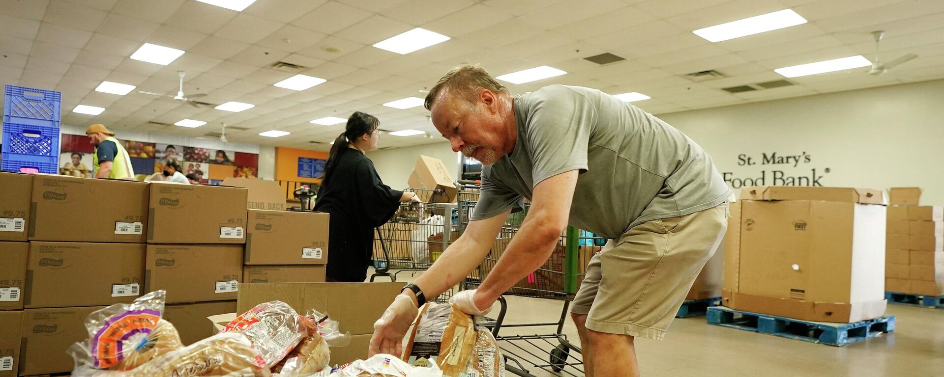 Voluntários enchem carrinhos de supermercado com alimentos para distribuição em veículos no drive through no Banco de Alimentos do St. Mary, em Phoenix, 29 de junho de 2022 - Sputnik Brasil, 1920, 19.12.2023
