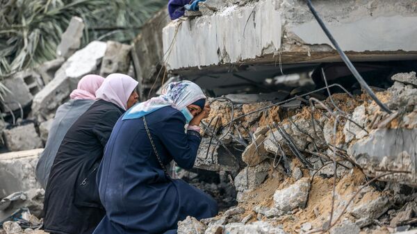 Mulheres palestinas choram onde se acredita que um parente esteja preso nos escombros após o bombardeio israelense em Rafah, no sul da Faixa de Gaza, em 21 de dezembro de 2023 - Sputnik Brasil