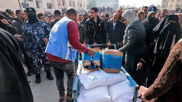 Trabalhadores da Agência das Nações Unidas de Assistência e Obras aos Refugiados da Palestina (UNRWA) distribuem rações de farinha e outros suprimentos às pessoas em um armazém da UNRWA em Rafah, no sul da Faixa de Gaza, em 12 de dezembro de 2023 - Sputnik Brasil