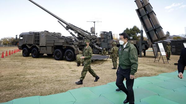 Fumio Kishida, primeiro-ministro do Japão (no centro à direita), passa junto de obuseiro autopropulsado Type 19 de 155 mm da Força de Autodefesa Terrestre do Japão (atrás à esquerda), e um míssil superfície-navio Type 12 (atrás à direita), no Campo da Força de Autodefesa Terrestre do Japão de Asaka em Tóquio, Japão, 27 de novembro de 2021 - Sputnik Brasil