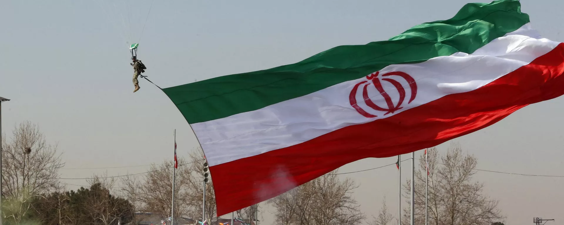 Um soldado pousando de paraquedas hasteia uma bandeira nacional iraniana enquanto as pessoas se reúnem para marcar o 45º aniversário da Revolução Islâmica em Teerã. Irã, 11 de fevereiro de 2024 - Sputnik Brasil, 1920, 12.04.2024