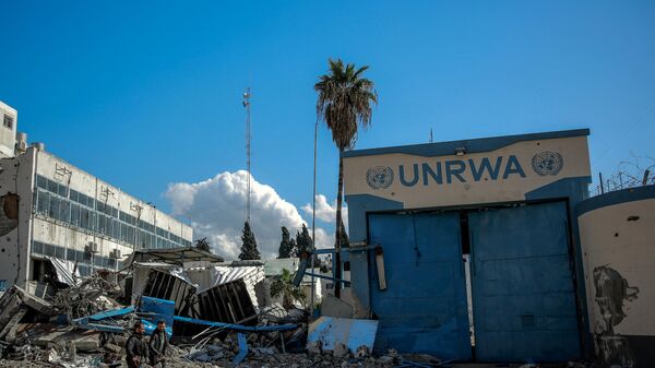 Pessoas passam pela sede danificada da Agência das Nações Unidas de Assistência e Obras para os Refugiados da Palestina no Oriente Próximo (UNRWA, na sigla em inglês), na cidade de Gaza, 15 de fevereiro de 2024 - Sputnik Brasil