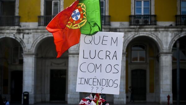 Homem coberto com fita adesiva segura uma bandeira portuguesa e um cartaz dizendo “Quem lucra com os incêndios?”, enquanto centenas de pessoas se juntam na Praça do Comércio, Lisboa, em 21 de outubro de 2017, para protestar contra a resposta do governo aos recentes fogos florestais em Portugal - Sputnik Brasil