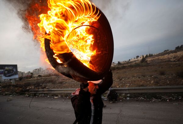Um palestino segura um pneu em chamas durante os confrontos com as tropas israelenses perto do povoado de Beit El, a pouca distância da cidade de Ramallah, na Cisjordânia, em 10 de dezembro de 2017 - Sputnik Brasil