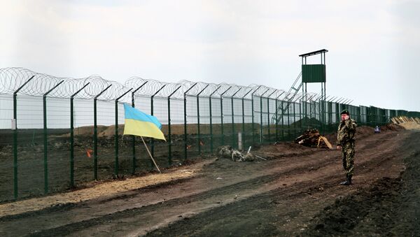 A Ukrainian border guard officer speaks on a phone near a national flag attached to the fence on the Ukrainian-Russian border near Hoptivka, Kharkiv region, eastern Ukraine - Sputnik Brasil