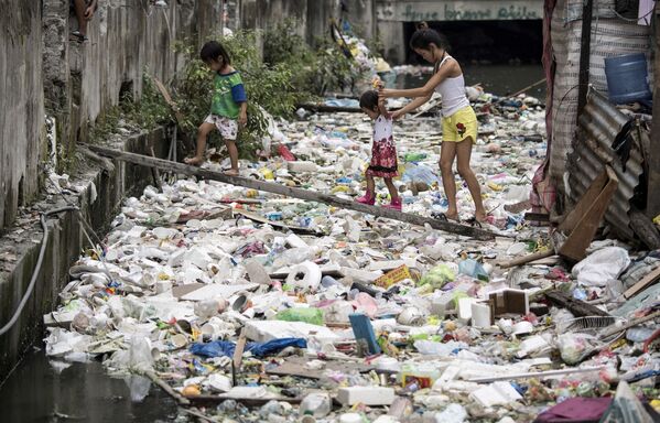 Residentes atravessam montes de lixo por uma tábua de madeira em Manila, nas Filipinas - Sputnik Brasil
