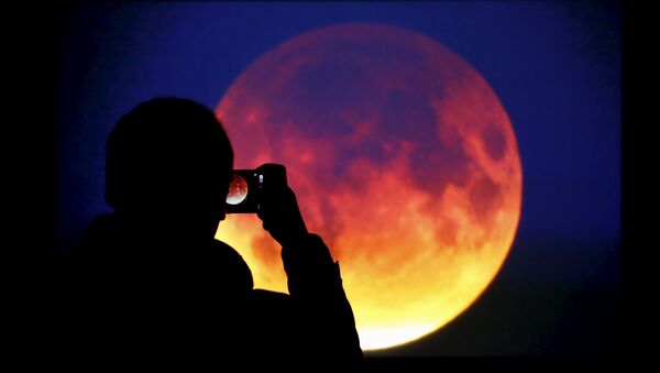 A man takes picture of the screen displaying the moon, appearing in a dim red colour, which is covered by the Earth's shadow during a total lunar eclipse in Warsaw, Poland September 28, 2015 - Sputnik Brasil