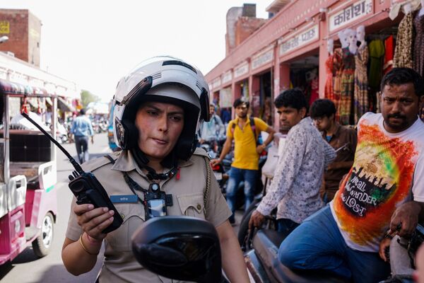 Uma policial escuta seu aparelho de rádio ao patrulhar um mercado em Jaipur, na Índia, em junho de 2017 - Sputnik Brasil