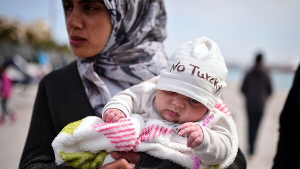 Refugiada síria segurando bebê de dois meses como refugiados e migrantes que partiram do campo de detenção de Chios, e acamparam no porto da cidade, organizando um protesto com seus filhos cantando 'No Turkey', em 3 de abril de 2016 - Sputnik Brasil