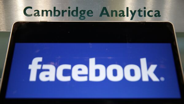 Laptop mostrando logotipo do Facebook é mantido ao lado de uma placa da Cambridge Analytica na entrada do prédio que abriga os escritórios da Cambridge Analytica, no centro de Londres. - Sputnik Brasil