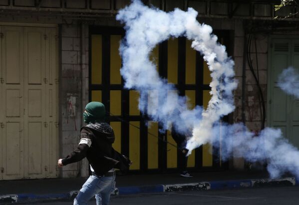Manifestante palestino atira uma botija de gás lacrimogêneo contra os soldados israelenses na cidade de Hebron - Sputnik Brasil