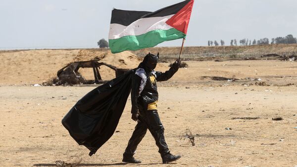 Manifestante palestino vestido de Batman segura a bandeira nacional perto da fronteira entre Israel e Faixa de Gaza - Sputnik Brasil