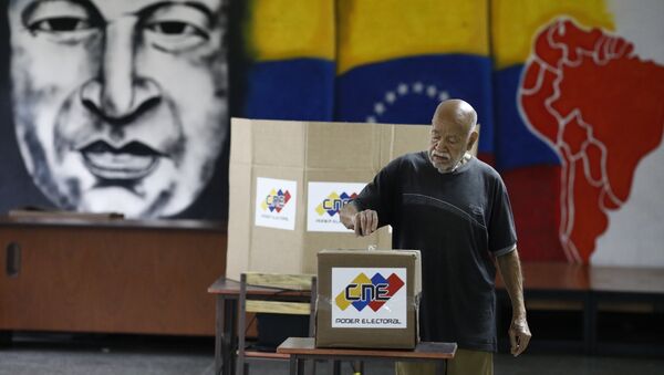 Com uma imagem do falecido presidente venezuelano Hugo Chávez, um cidadão venezuelano deposita seu voto em uma seção de votação durante a eleição presidencial em Caracas, Venezuela, em 20 de maio de 2018. - Sputnik Brasil