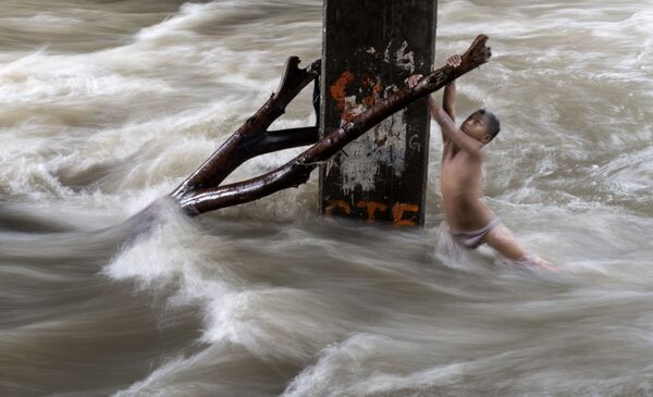 Uma criança segura um tronco debaixo de uma ponte parcialmente submersa depois das chuvas fortes em Manila, nas Filipinas - Sputnik Brasil