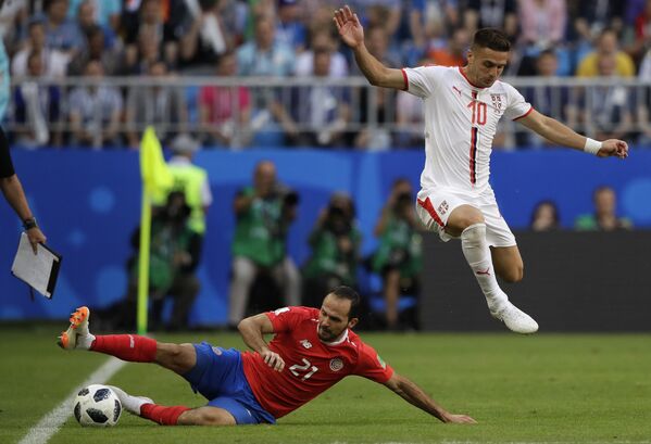 Jogador da Sérvia, Dusan Tadic, salta sobre o costa-riquenho Marcos Urena, que desliza sobre o gramado durante o jogo entre Sérvia e Costa Rica, na Copa do Mundo de 2018. - Sputnik Brasil
