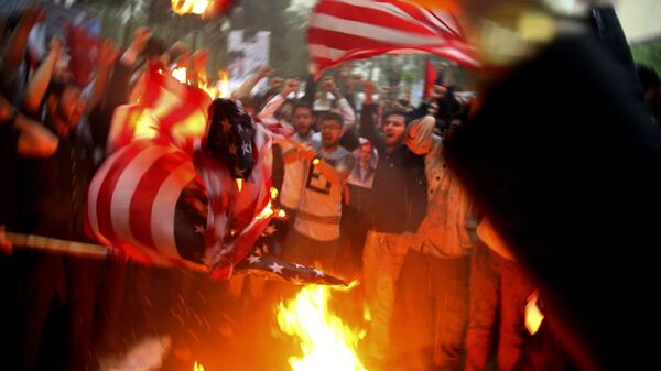 Manifestantes iranianos queimam bandeiras dos EUA durante protesto em frente a antiga embaixada dos Estados Unidos em resposta à decisão de Donald Trump, então presidente dos EUA, de desistir do acordo nuclear e renovar sanções a Teerã - Sputnik Brasil